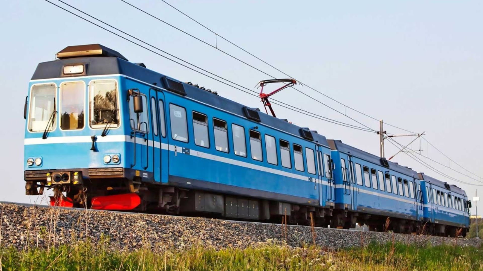 A blue train moves swiftly along the tracks under a clear sky.