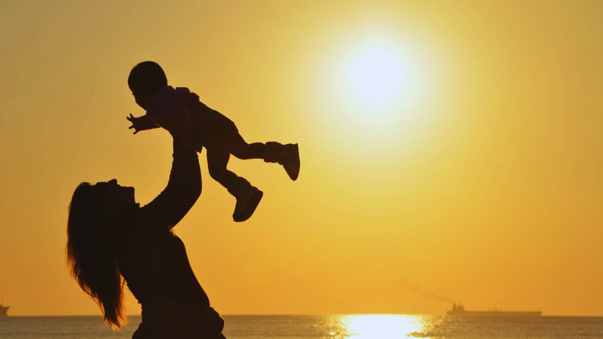 At sunset, a woman holds a child aloft, capturing a moment of joy and warmth.