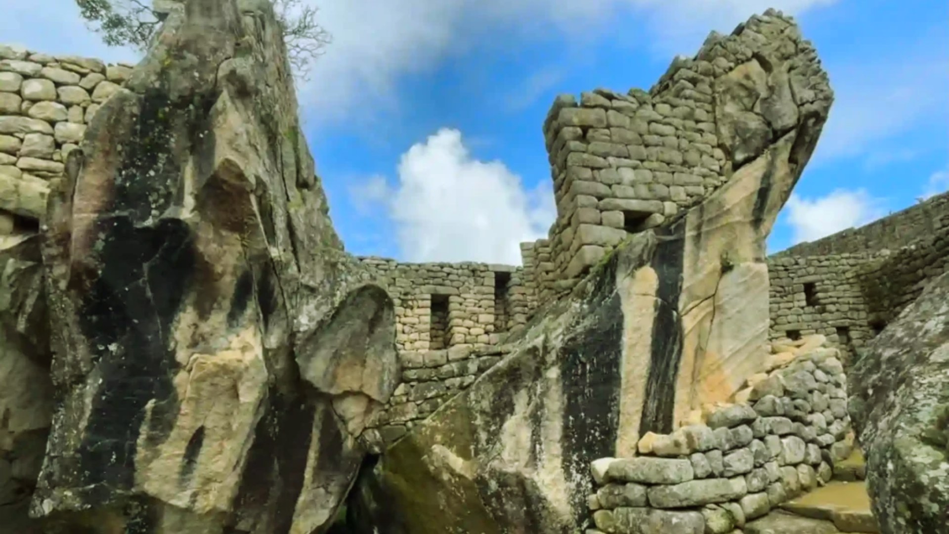 Ancient stone ruins featuring tall, weathered walls and large, irregular boulders under a blue sky with scattered clouds, conveying a sense of history and mystery.