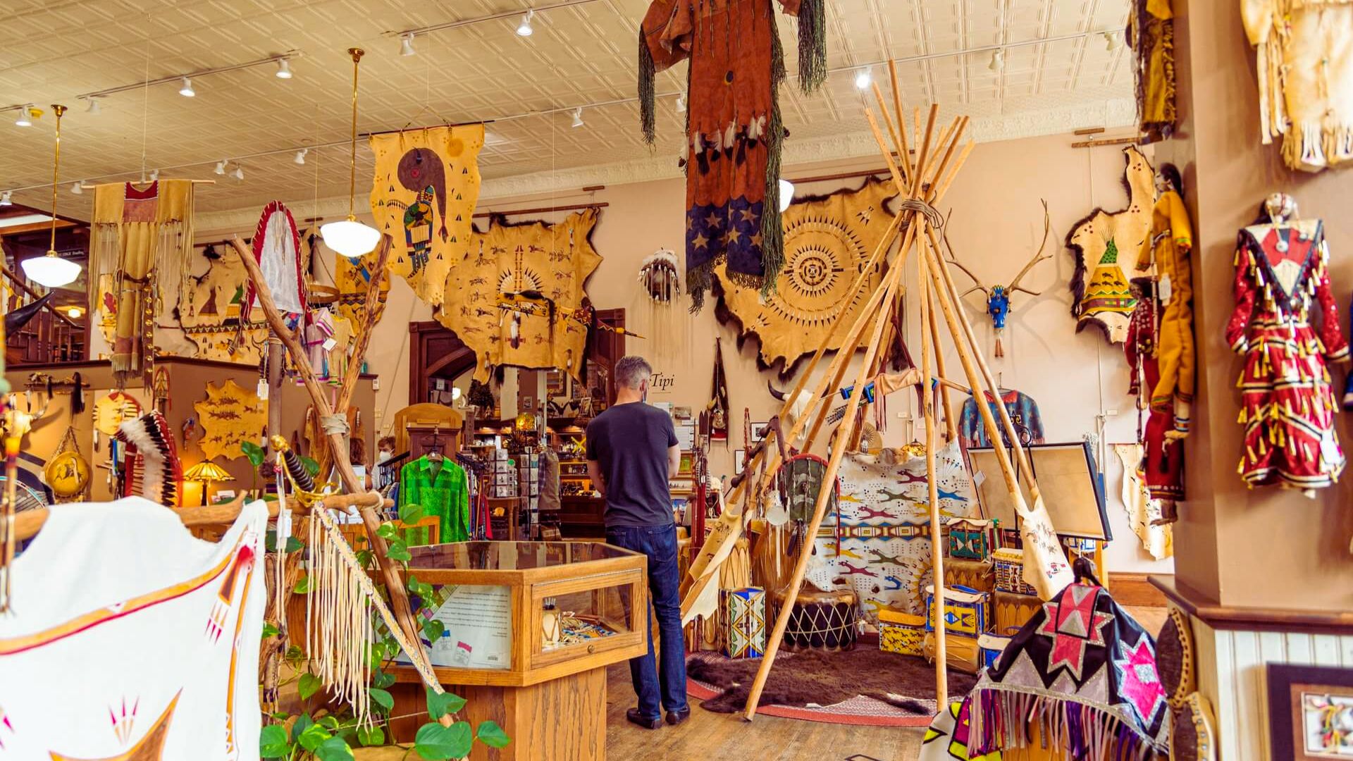 A man examines a display of Native American artifacts in a museum setting, showcasing cultural history and craftsmanship.