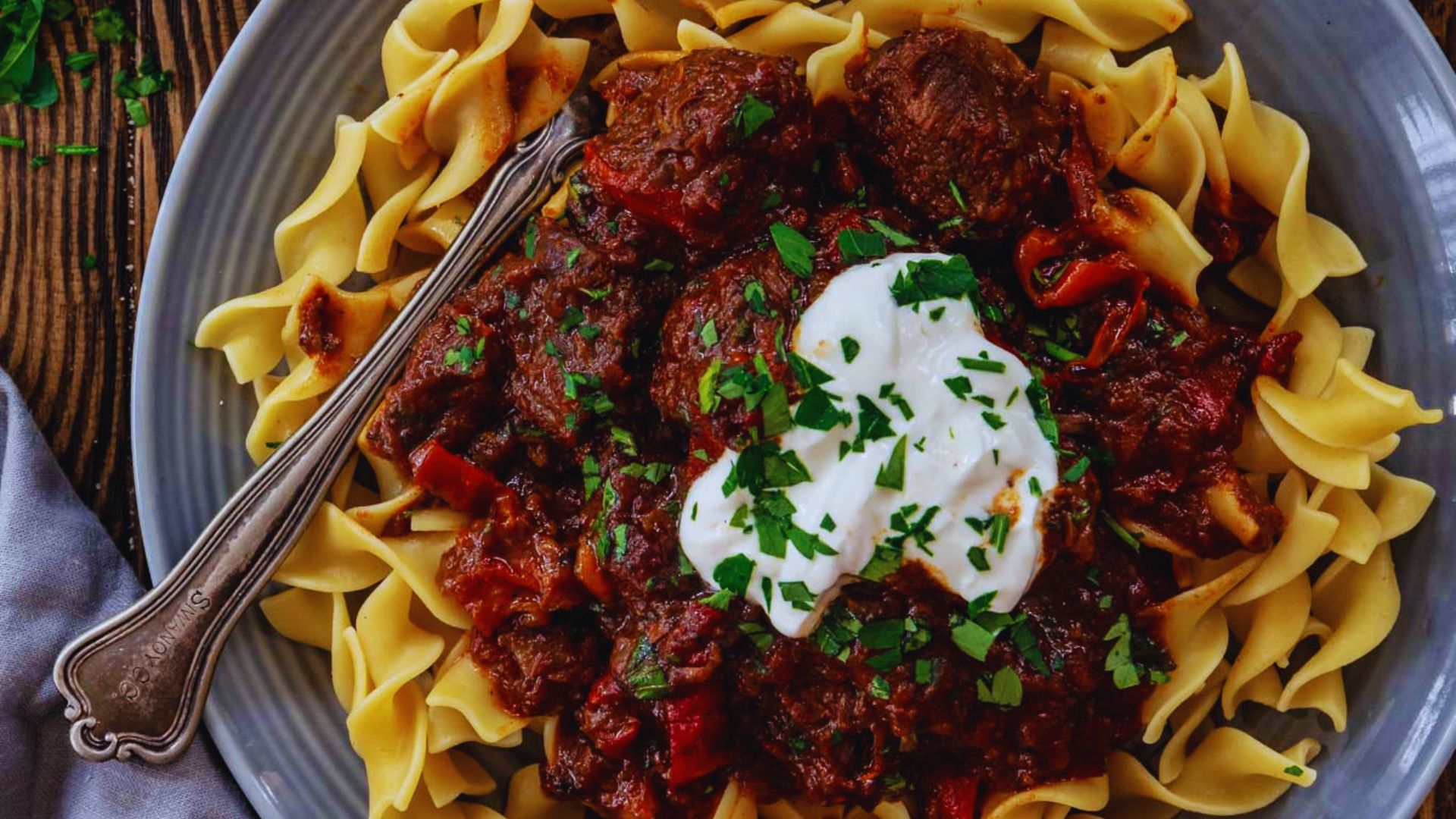 Meatballs in tomato sauce served over pasta, garnished with a dollop of sour cream.