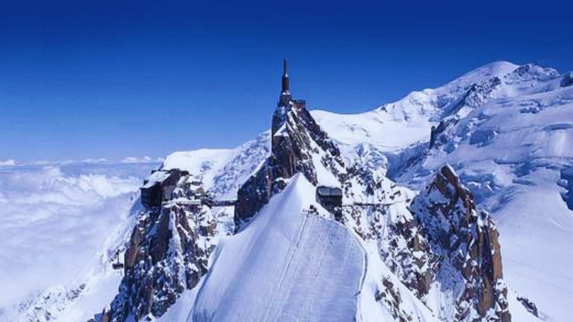 A majestic mountain peak featuring a quaint church perched at its summit against a clear blue sky.