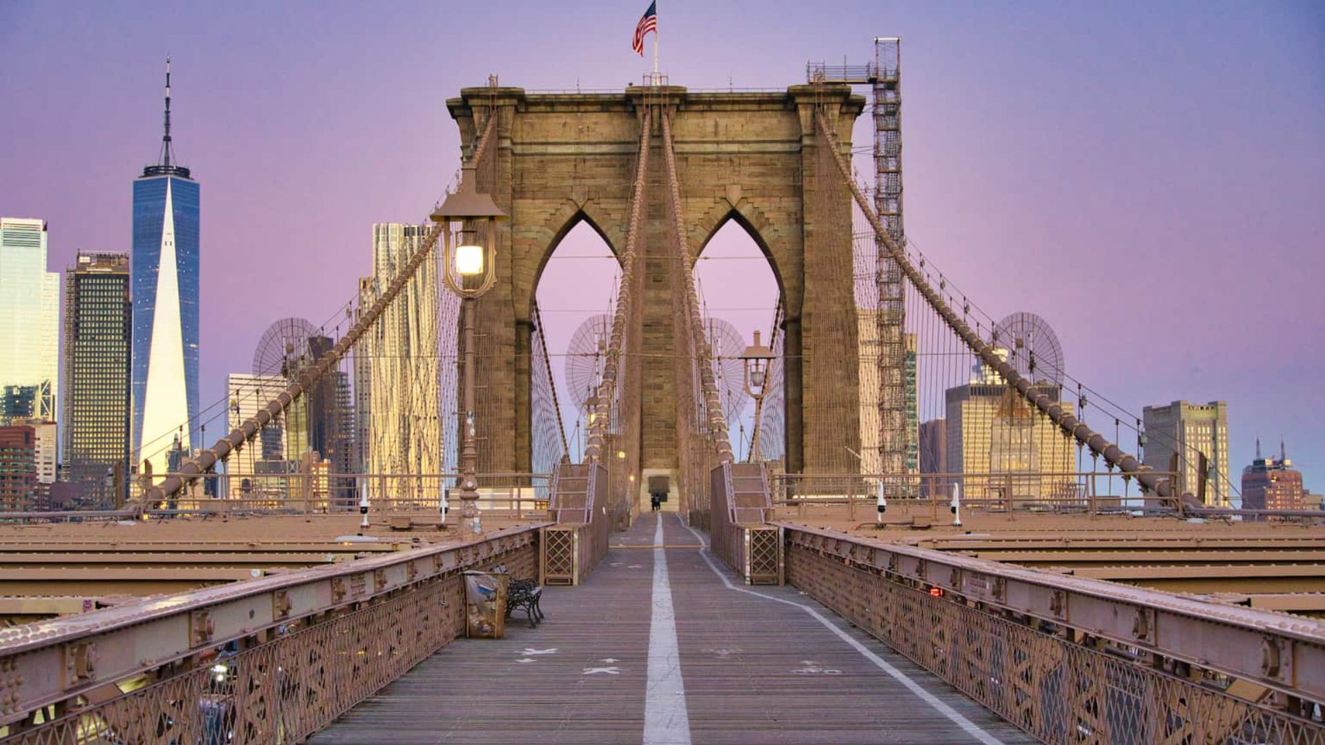 The Brooklyn Bridge at sunset, with the city skyline illuminated in the background, creating a picturesque urban scene.