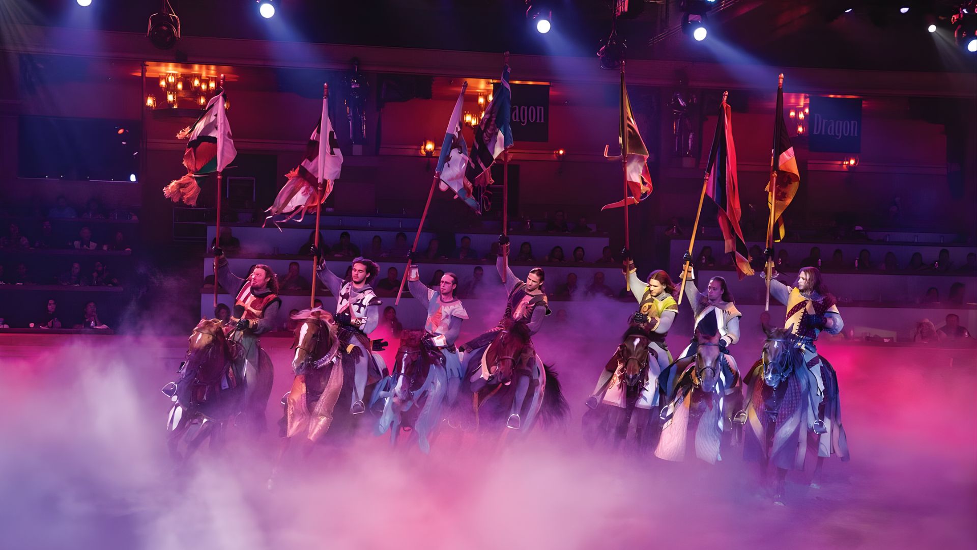 A group of dancers in colorful costumes performing on stage, holding vibrant flags as part of their routine.