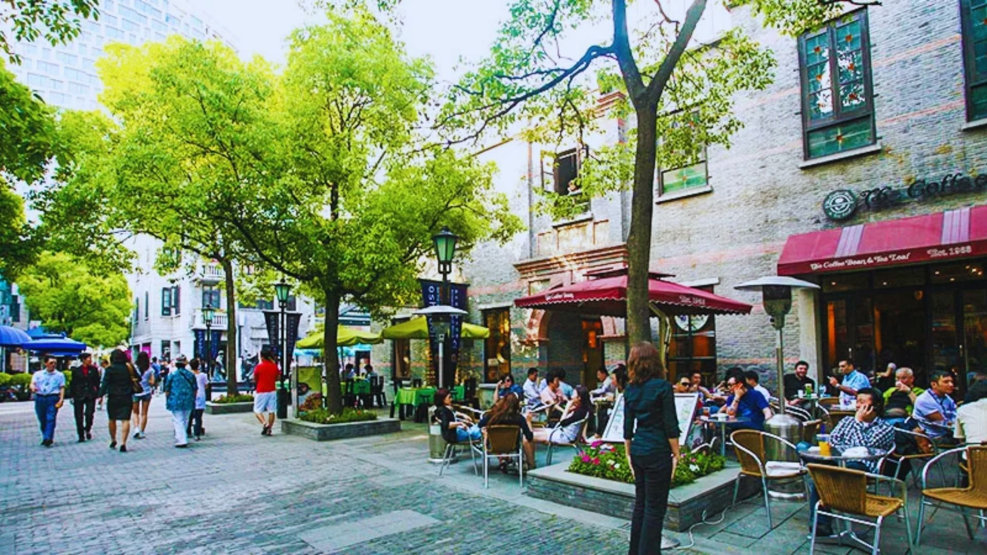 People seated at tables along a bustling city street, enjoying food and conversation in an outdoor setting.