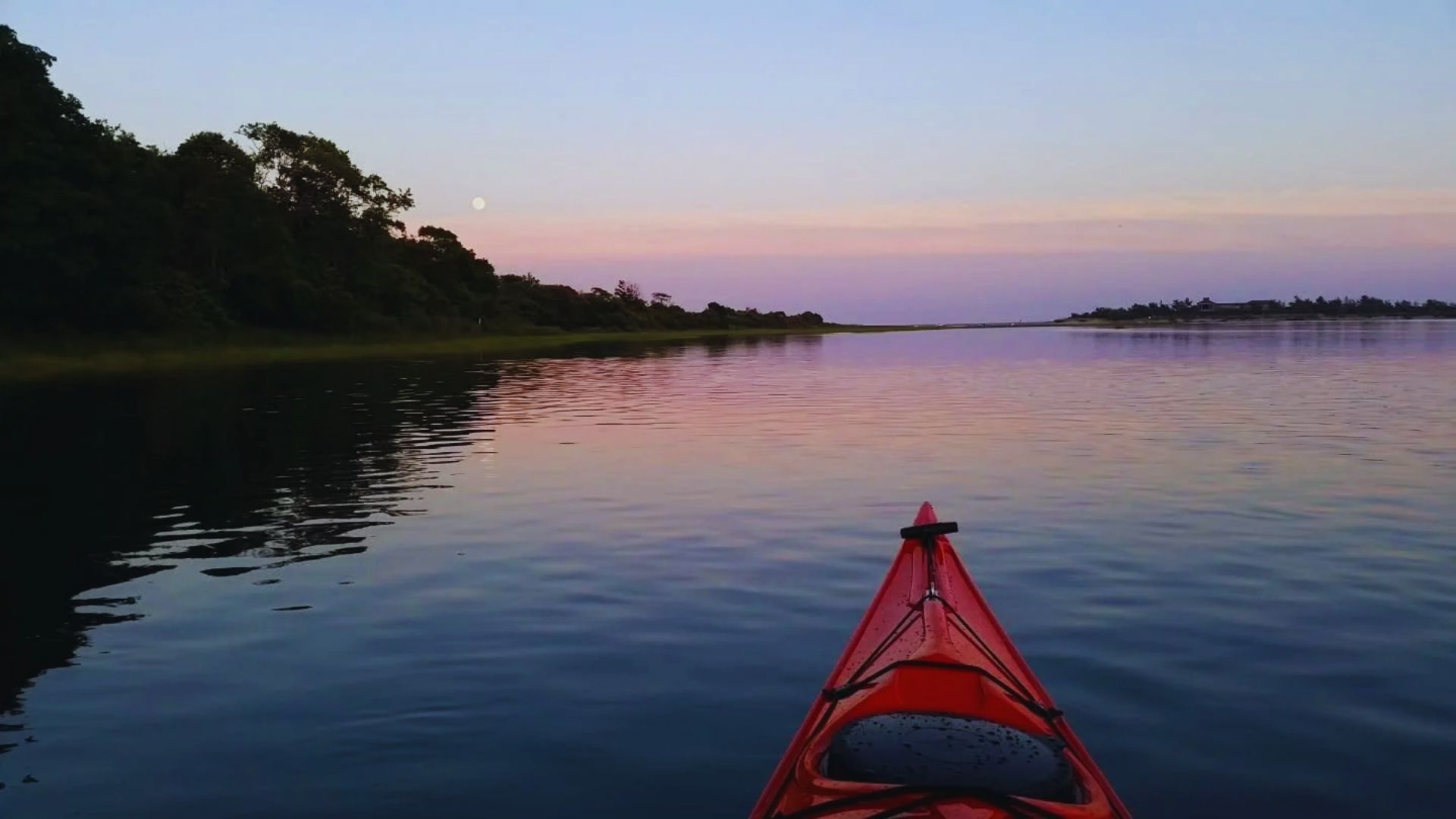 kayak floats on calm water during a vibrant sunset, with warm hues reflecting on the surface.
