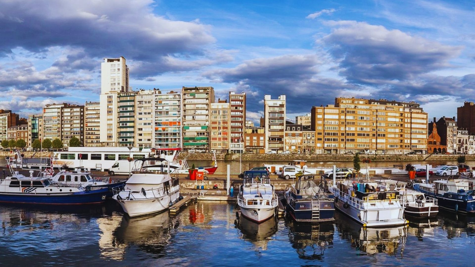 Boats are docked in a harbor with various buildings visible in the background under a clear blue sky.