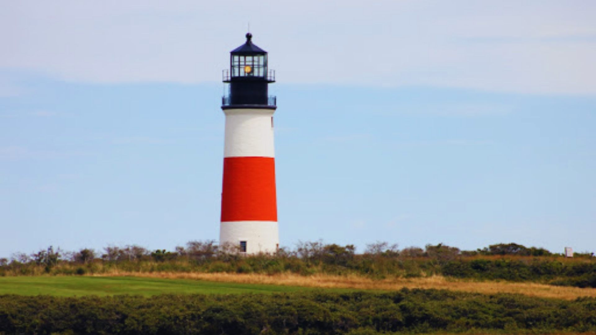 A lighthouse featuring a red and white striped tower against a clear blue sky.