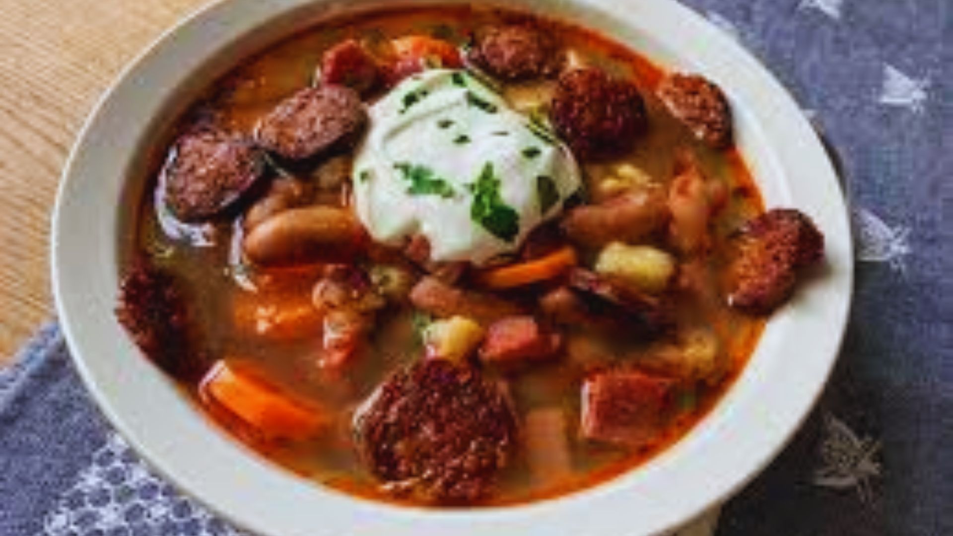 A bowl of chorizo and bean soup topped with a dollop of sour cream, garnished with herbs.