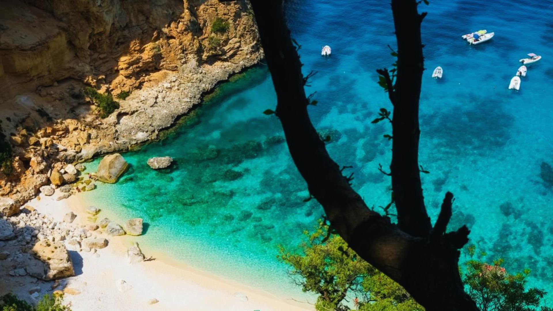 A secluded beach with golden sand and clear turquoise waters framed by rocky cliffs. Boats float nearby, evoking a serene and idyllic summer vibe.
