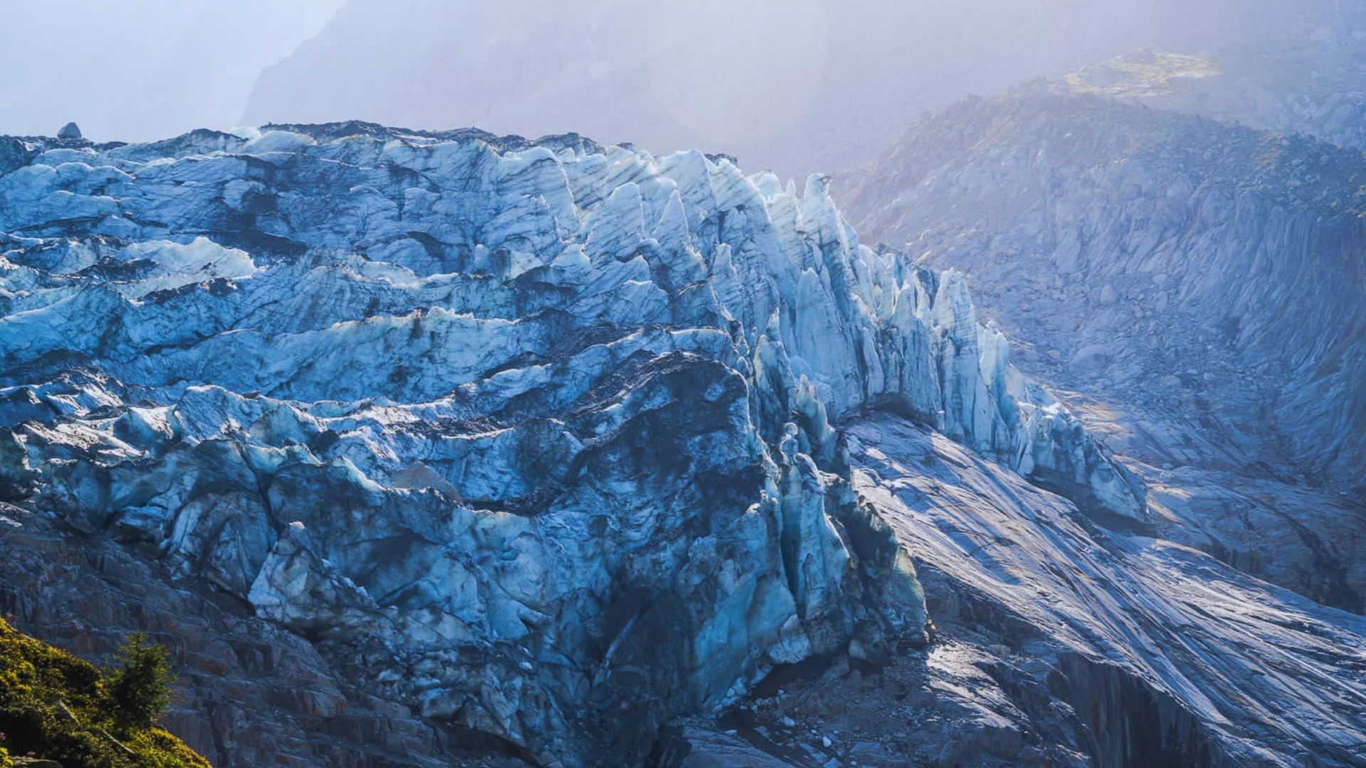 A large glacier glistens in the sunlight, showcasing its icy blue hues and rugged texture against a clear sky.