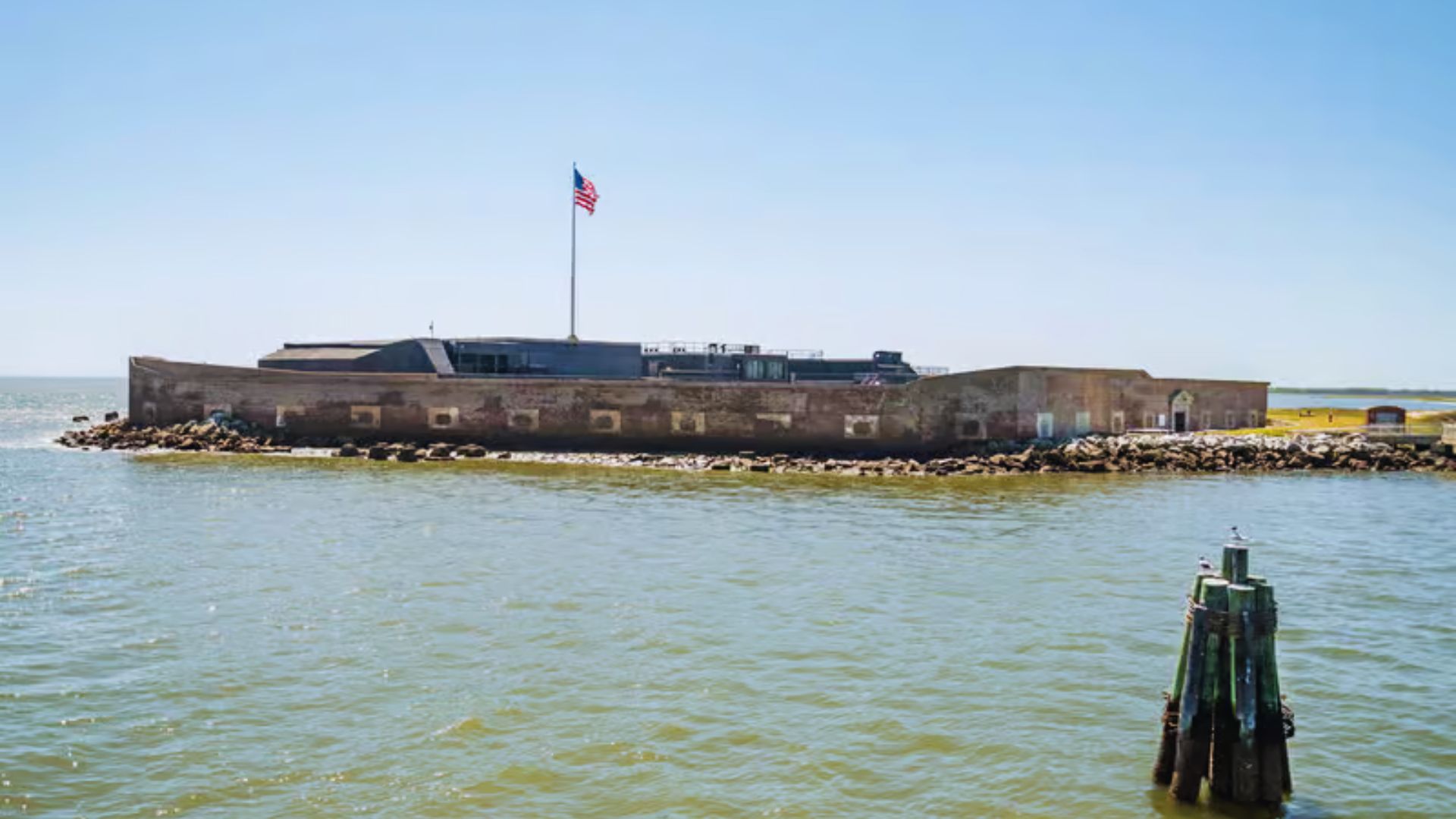 A fort situated on the water, featuring a flag waving atop its structure against a clear sky.