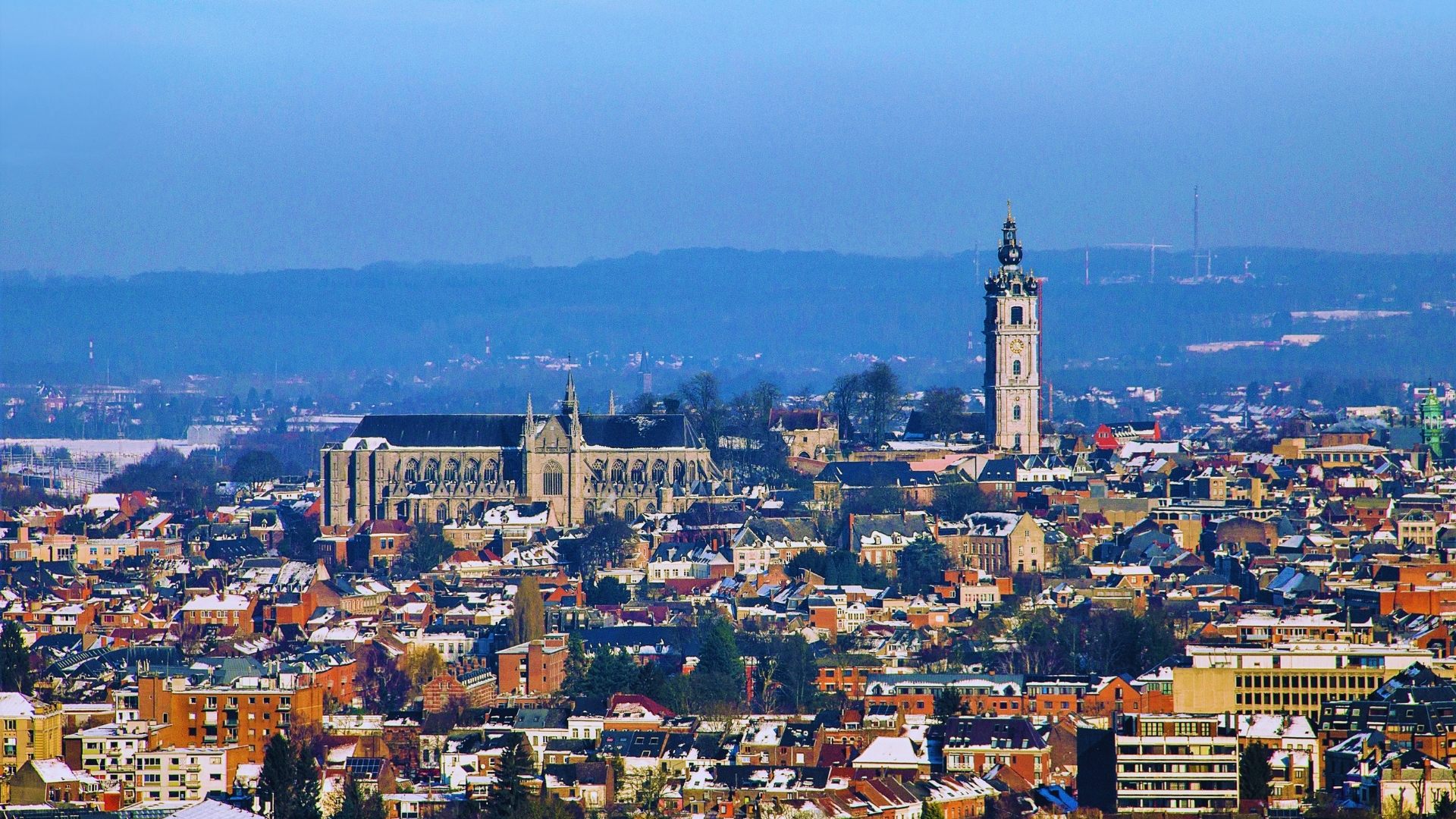 A city skyline featuring a prominent church tower in the background against a clear blue sky.
