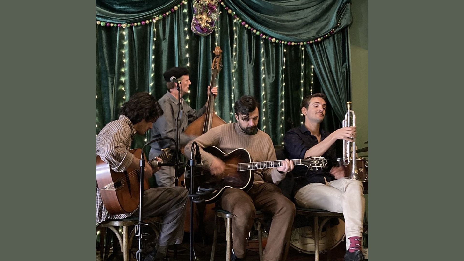 A group of men playing various instruments on stage in front of a decorative curtain.