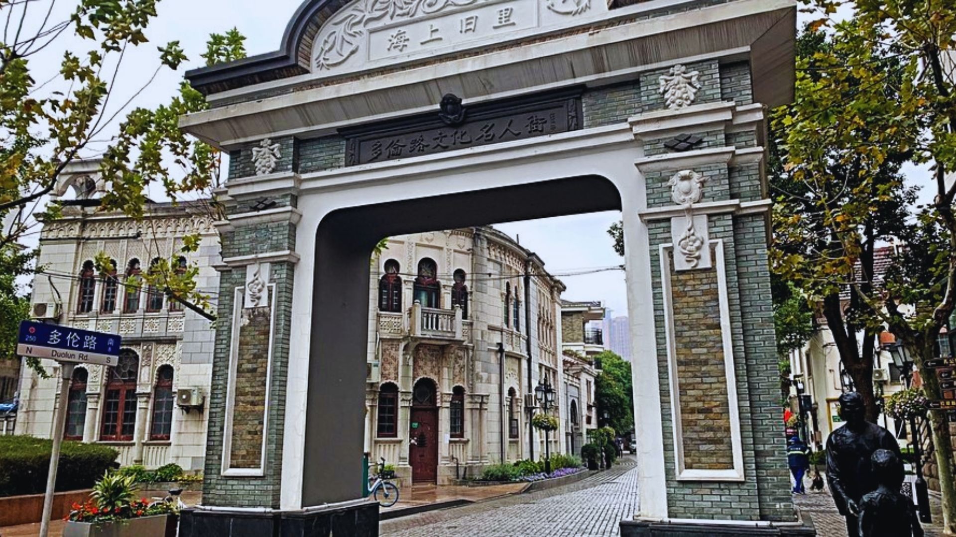 A decorative gate stands prominently in the center of a bustling city street, surrounded by buildings and pedestrians.