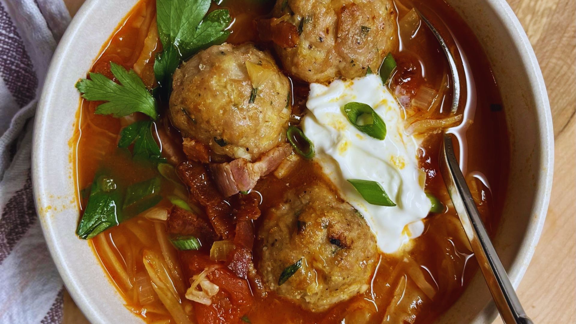 A bowl of turkey meatball soup with noodles, garnished with herbs and served steaming hot.