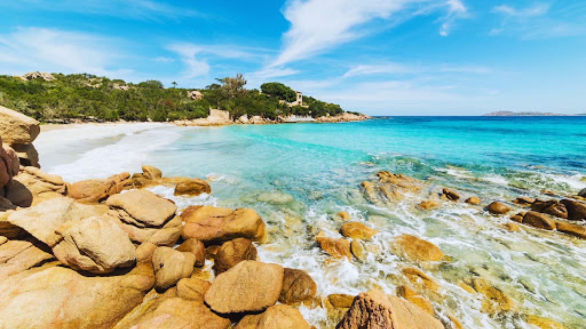 A serene beach scene with turquoise waters gently crashing onto rocky shores. Lush greenery and clear blue skies create a tranquil, inviting atmosphere.