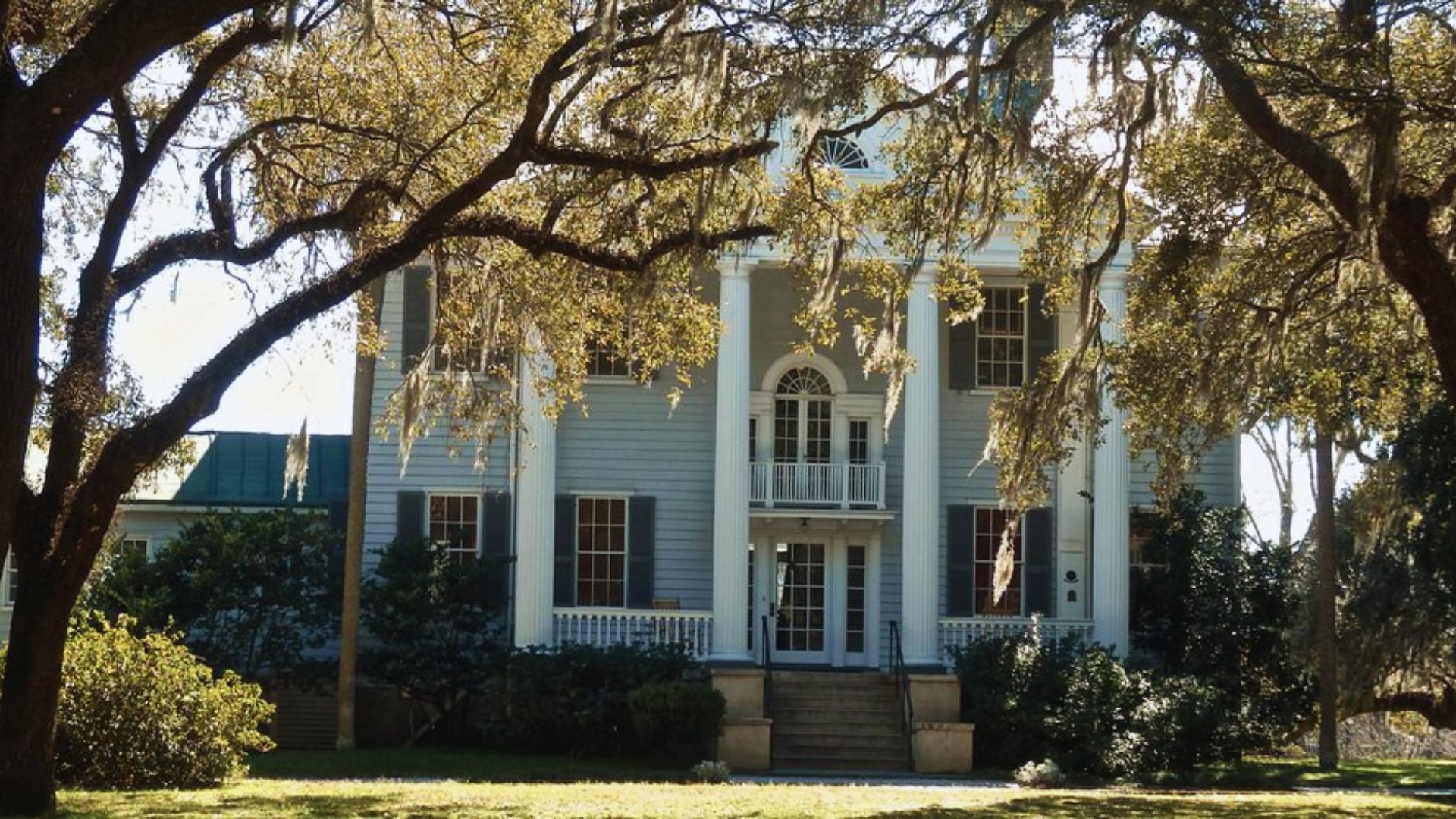 A large white house featuring a spacious porch, surrounded by trees in a serene outdoor setting.