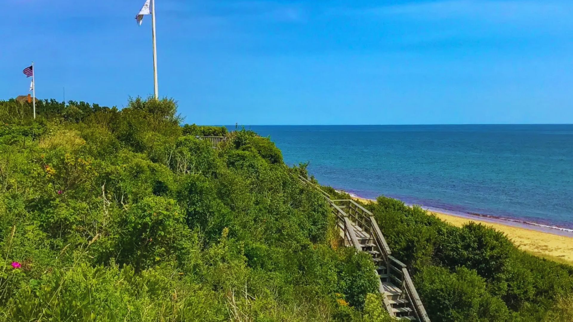 A sandy beach with colorful flags and a winding path leading to the ocean waves in the background.