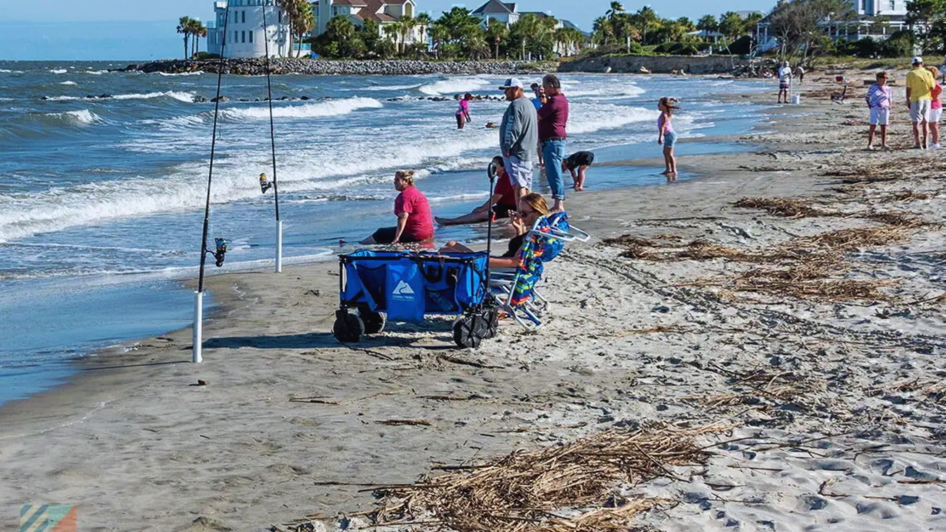 People fishing on the beach, with a cart and a boat nearby, enjoying a sunny day by the water.