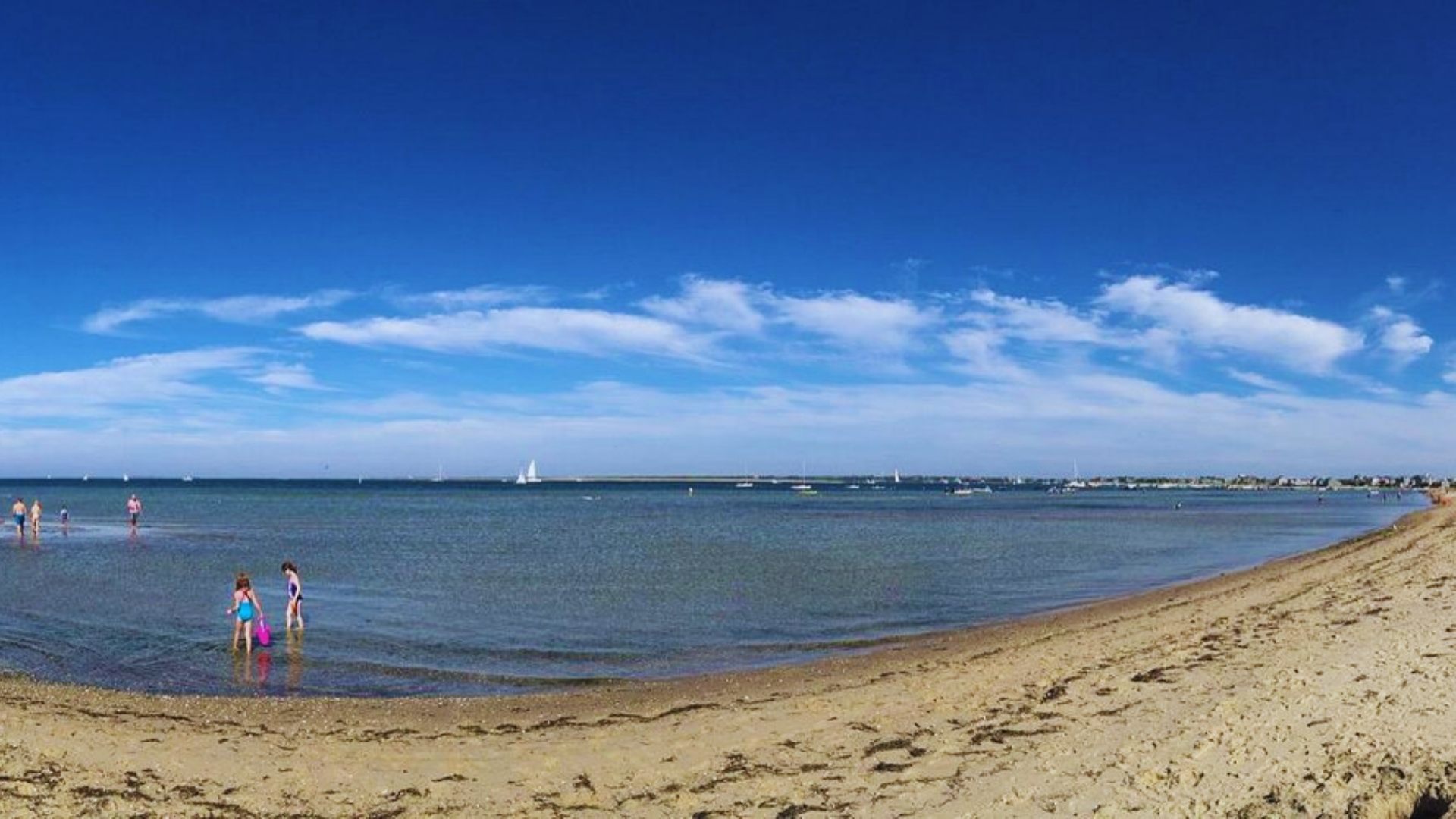 A sunny beach scene with people swimming in the clear water, enjoying the warm weather and vibrant atmosphere.