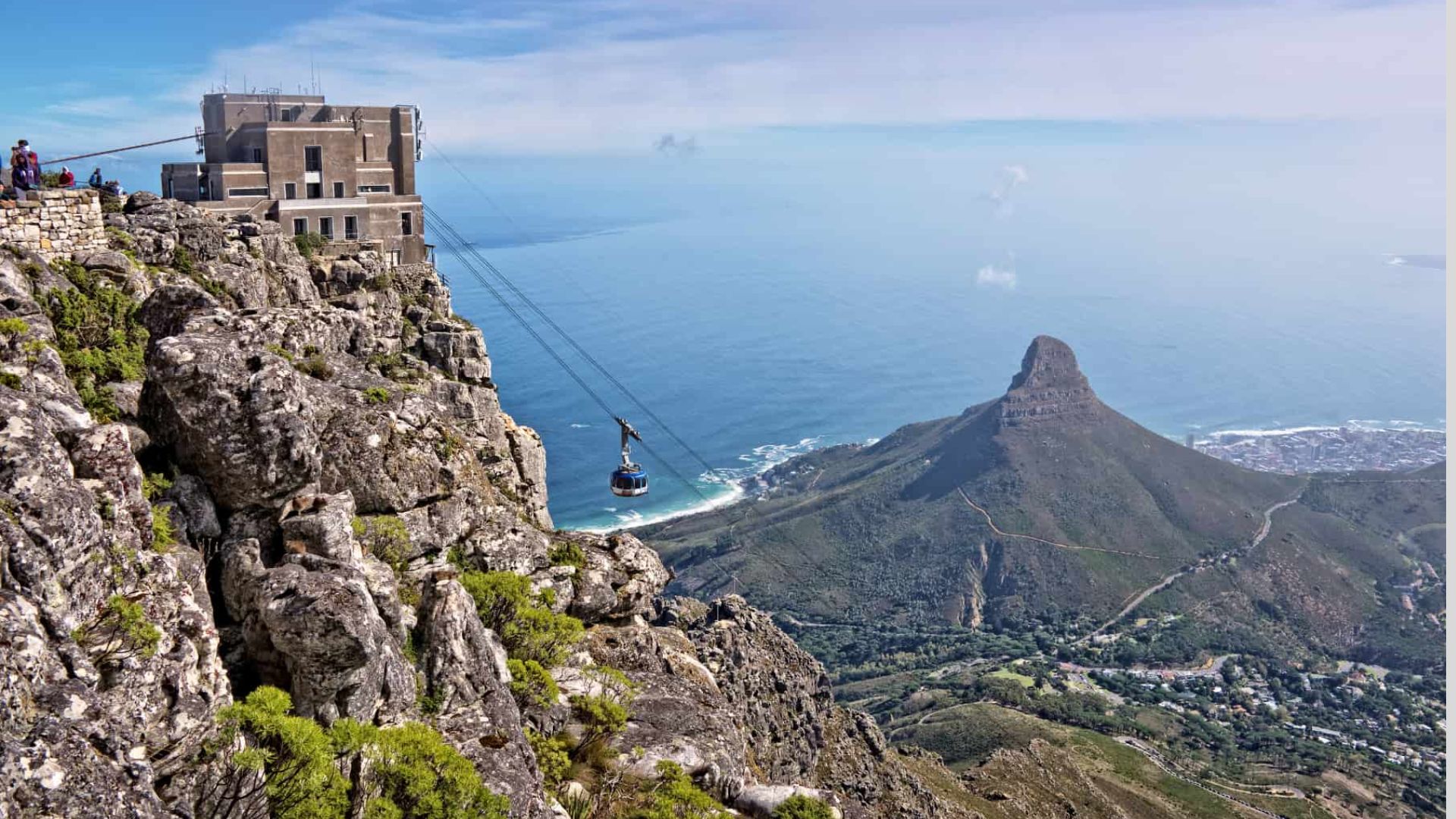 A cable car ascending Table Mountain, surrounded by lush greenery and a clear blue sky.