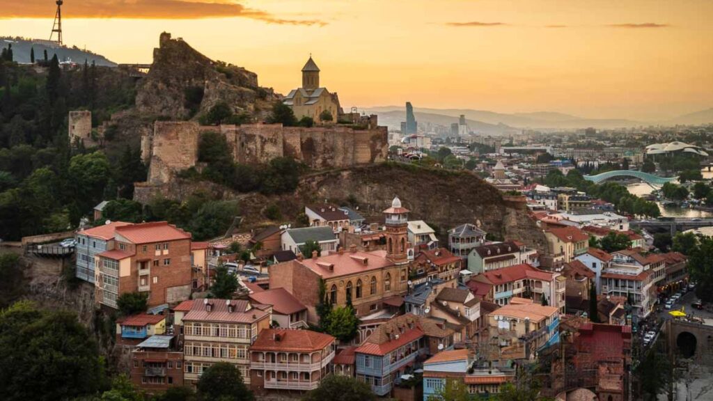 . Tbilisi skyline at sunset, showcasing vibrant colors reflecting off buildings and the Kura River.