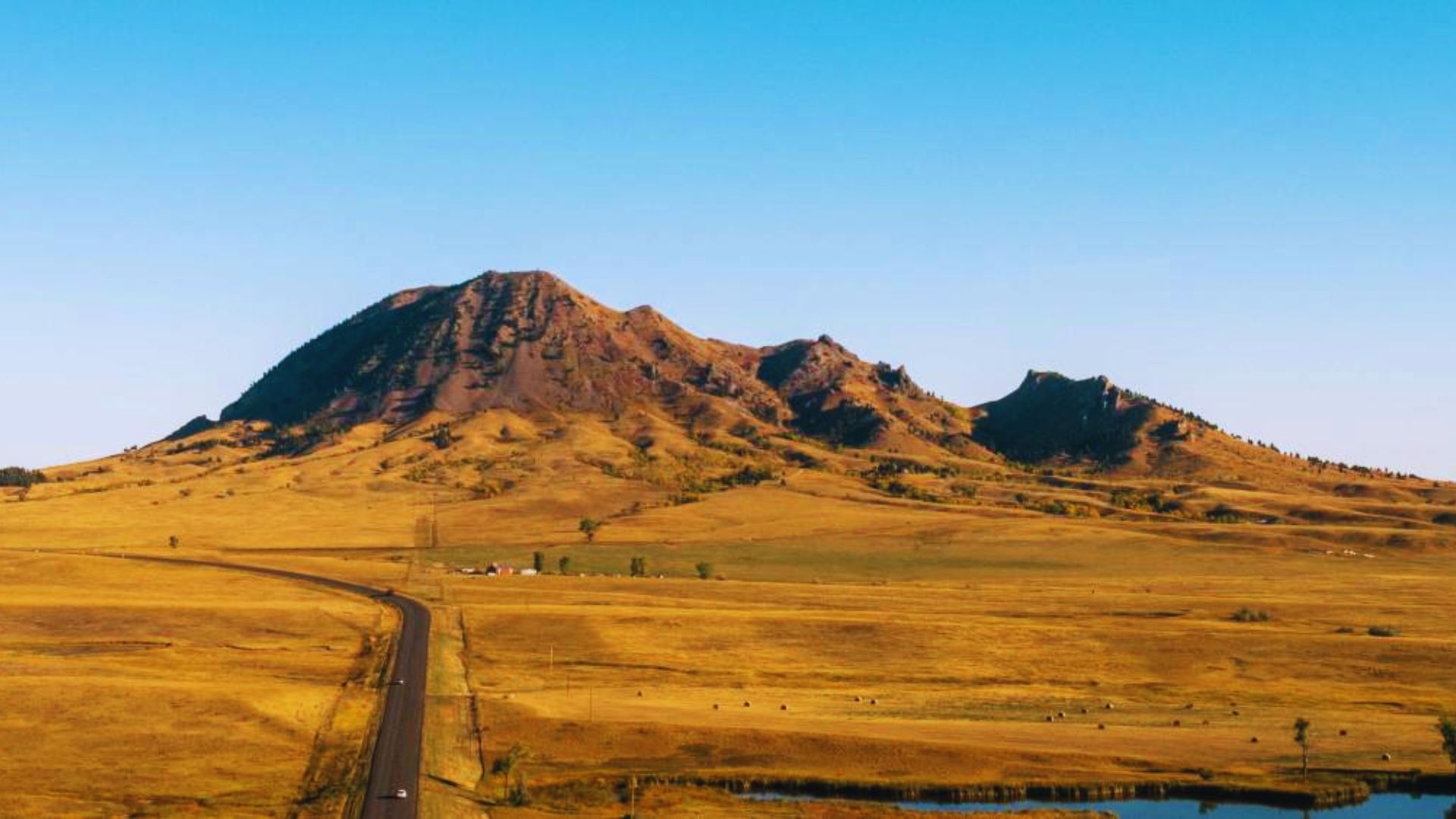 A road stretches through a grassy plain, with a mountain rising majestically in the background.