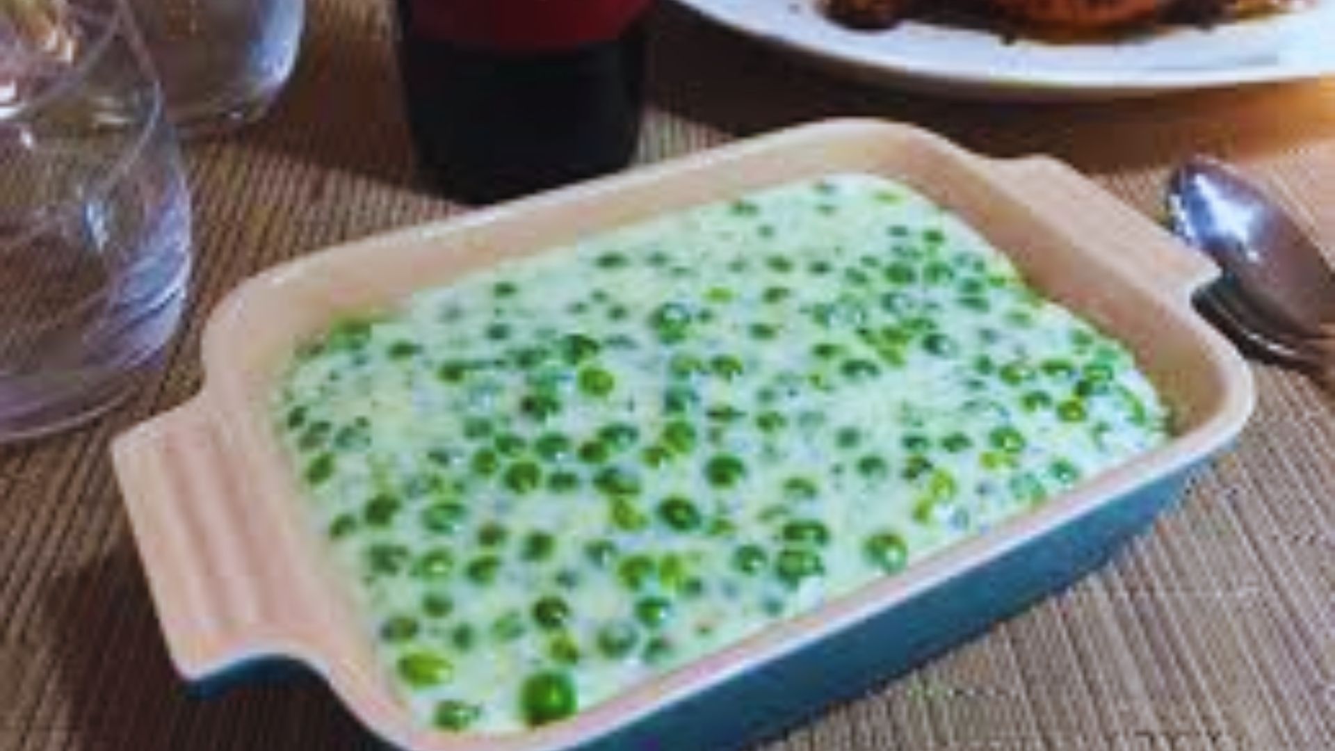 A bowl of green peas next to a plate of grilled chicken, arranged on a wooden table.