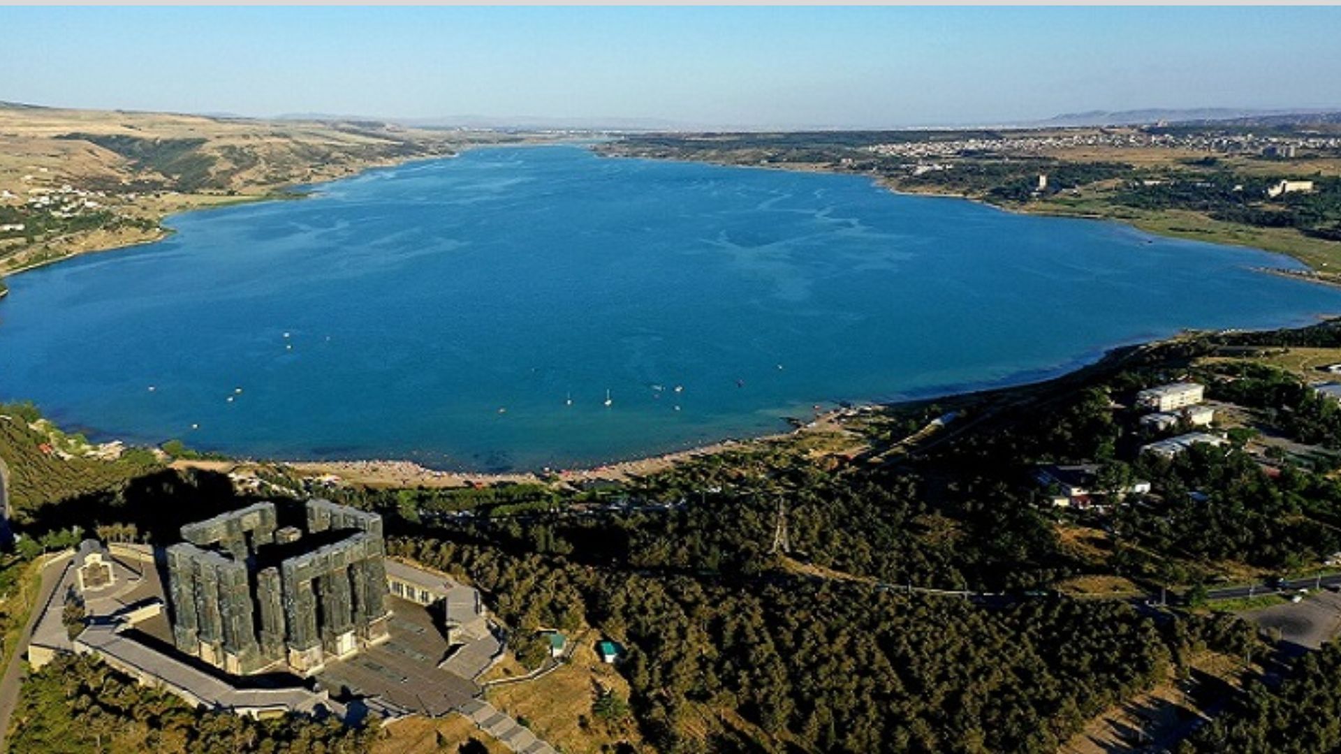 Aerial view showcasing a serene lake surrounded by a bustling cityscape under a clear blue sky.