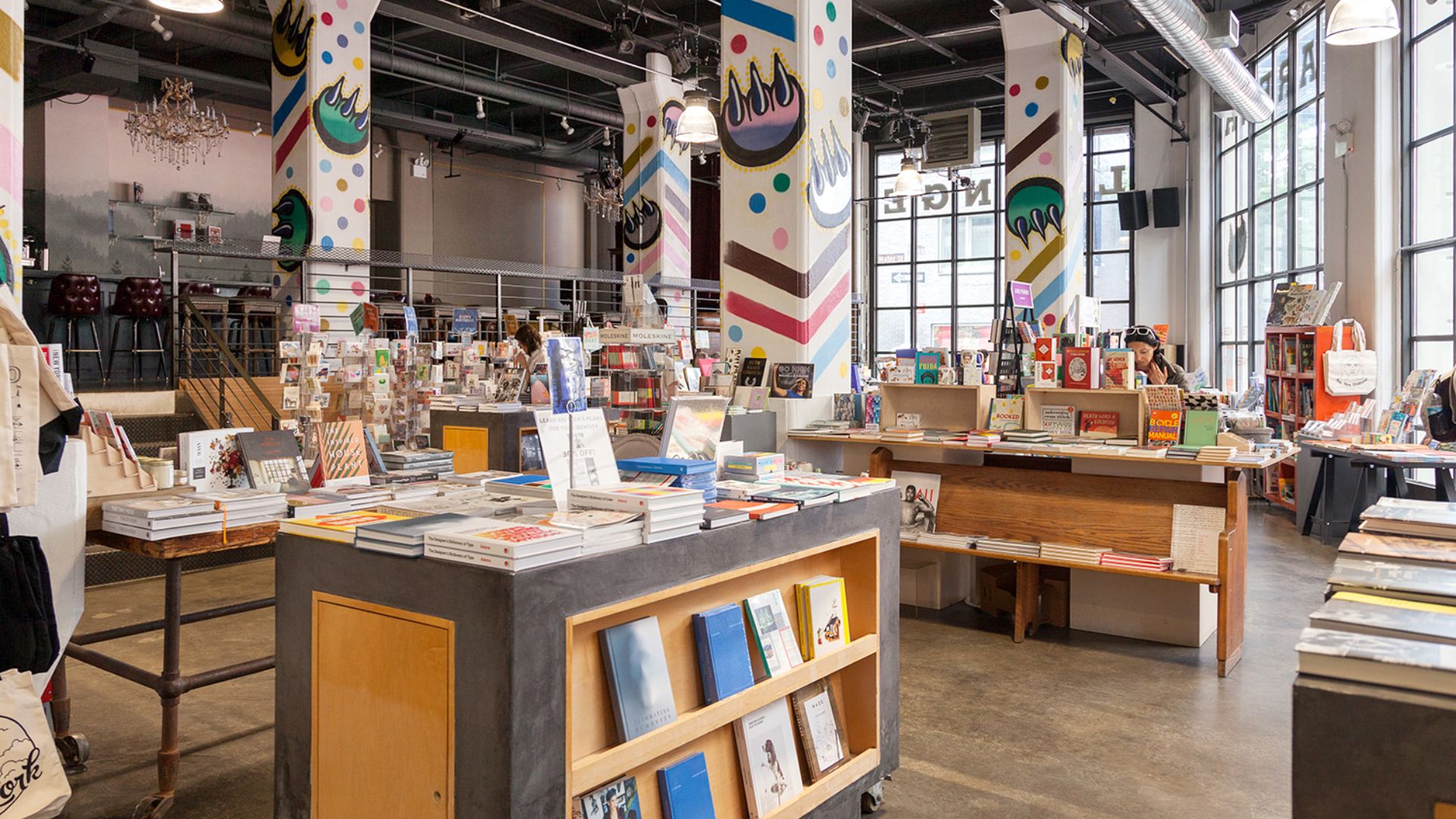 A busy bookstore filled with shelves of books and numerous people browsing and reading throughout the space.