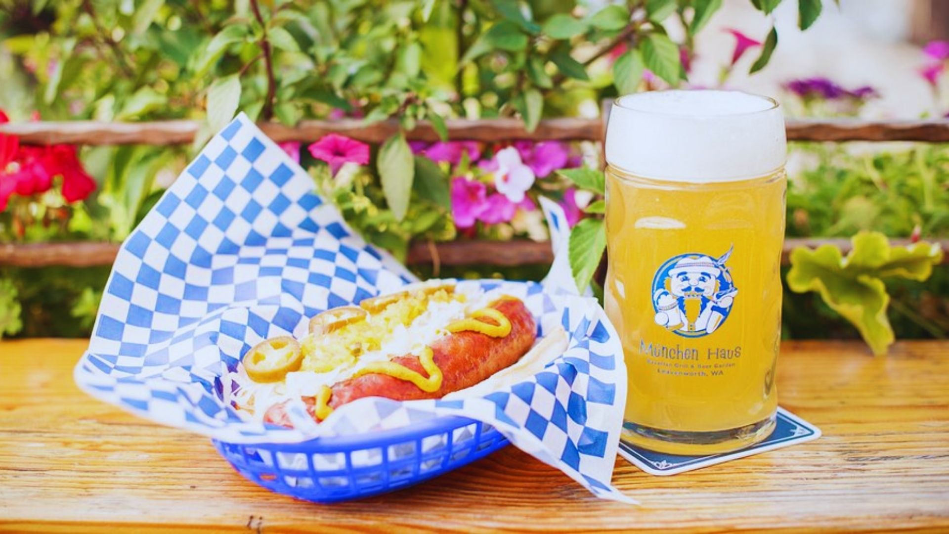 A hot dog and a beer sit on a table adorned with colorful flowers, creating a vibrant outdoor dining scene.