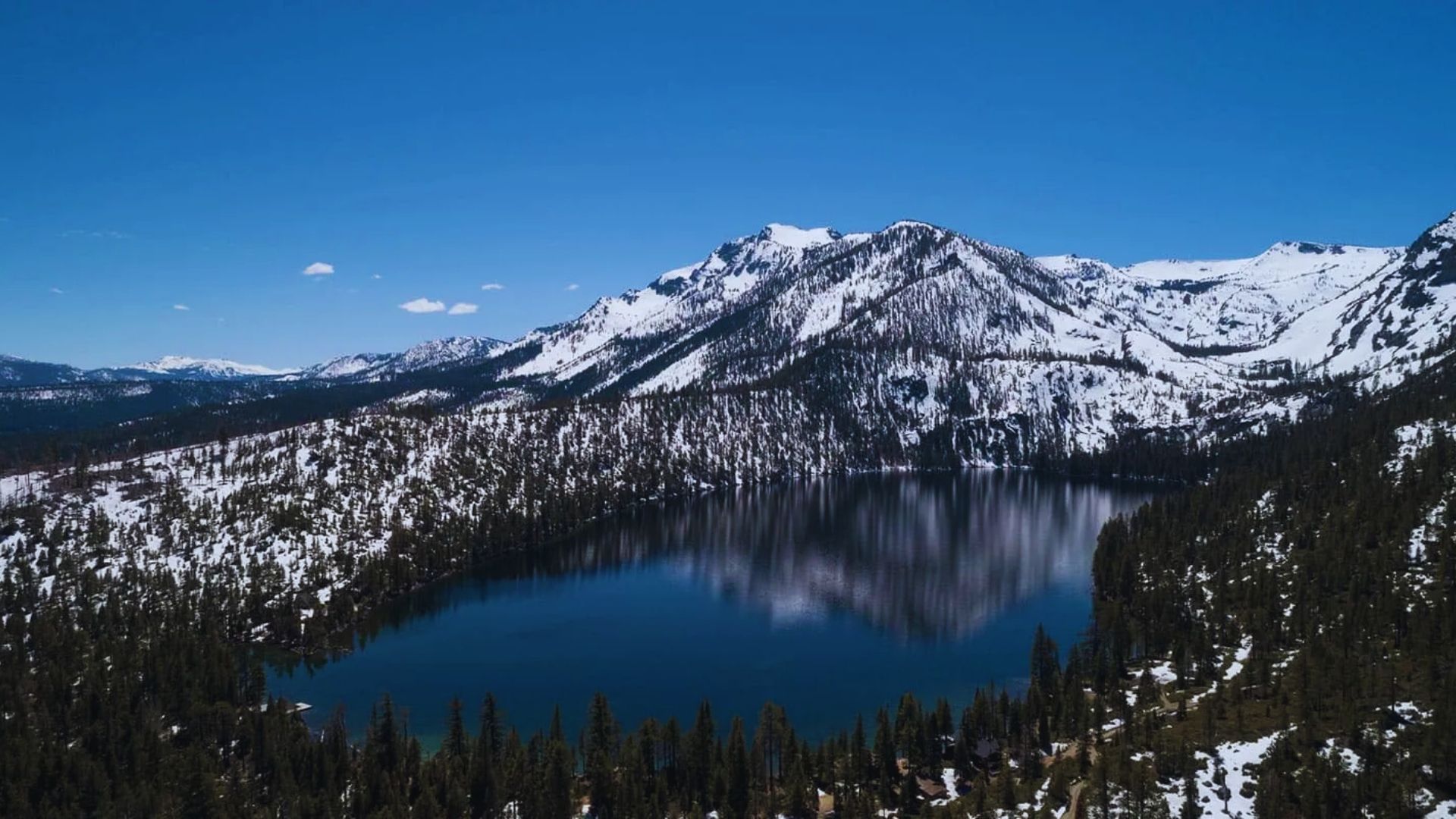 A serene lake nestled among majestic snow-covered mountains under a clear blue sky.