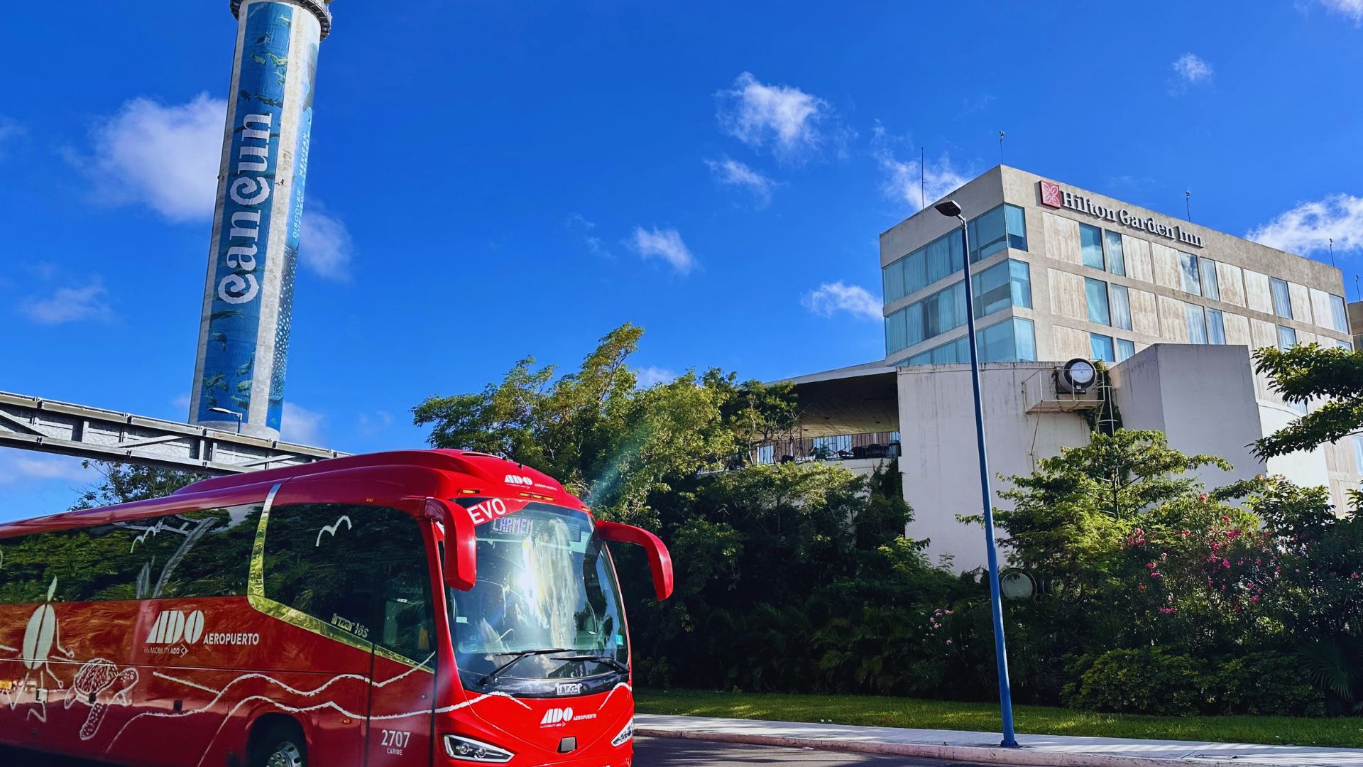 A red bus drives past a tall building, showcasing urban transportation against a city skyline.
