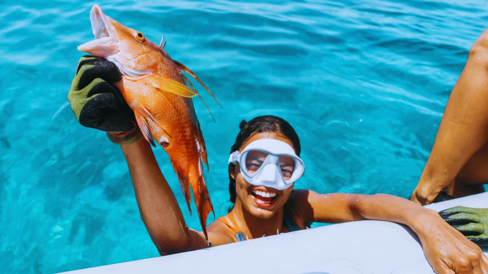 A woman wearing a snorkel mask holds a fish, smiling while enjoying her underwater adventure.
