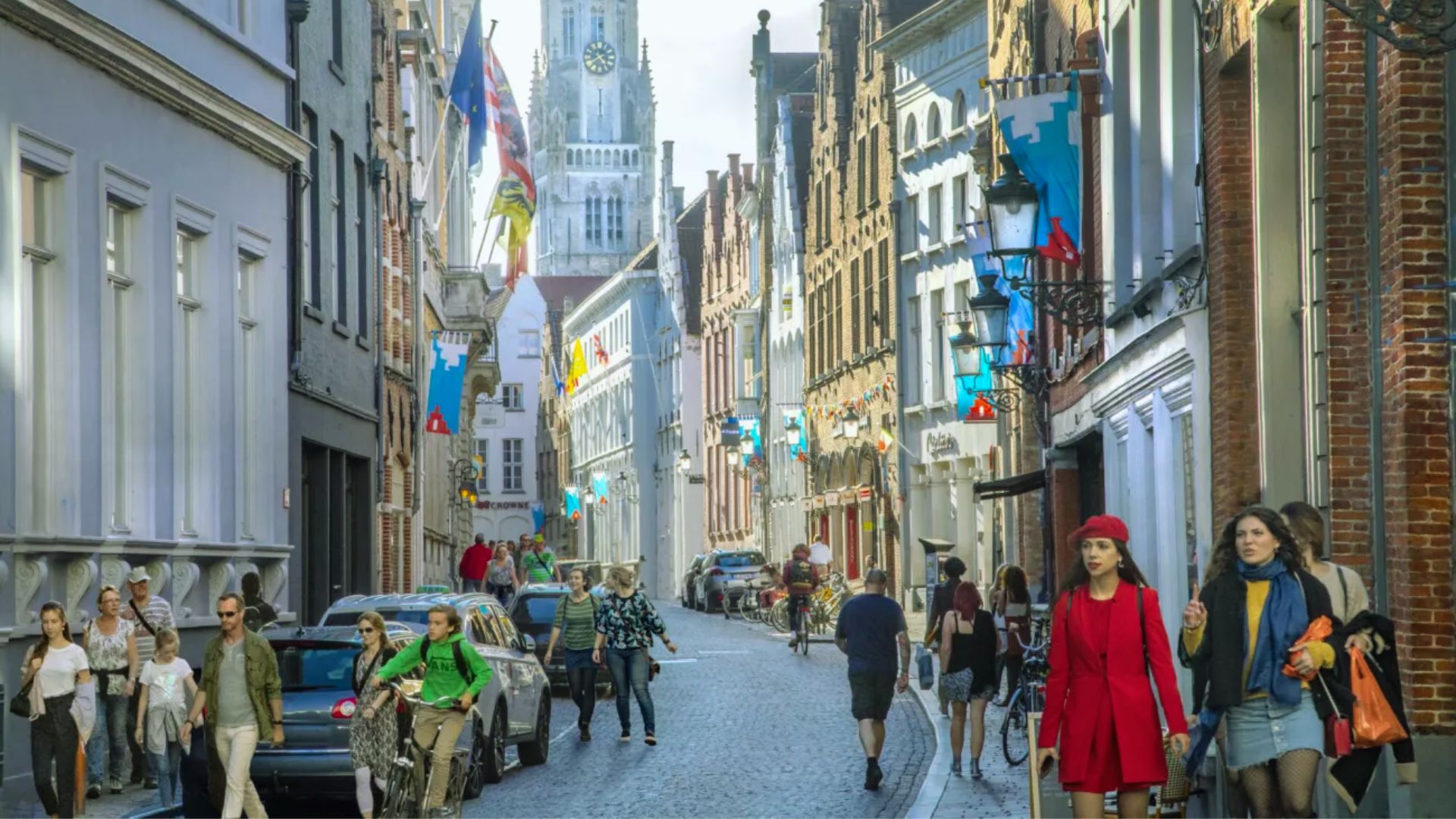 A group of people walking along a narrow city street lined with buildings and storefronts.