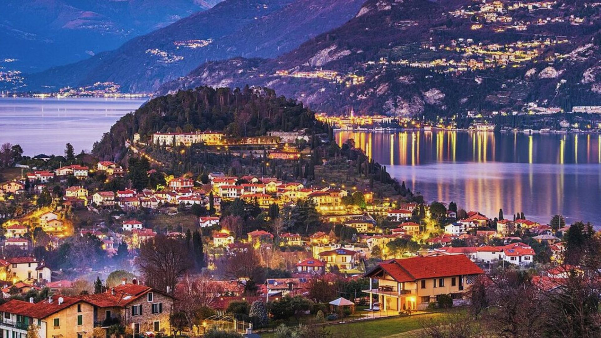 Night view of Lake Como, with the town aglow, highlighting its picturesque buildings and serene waterfront.