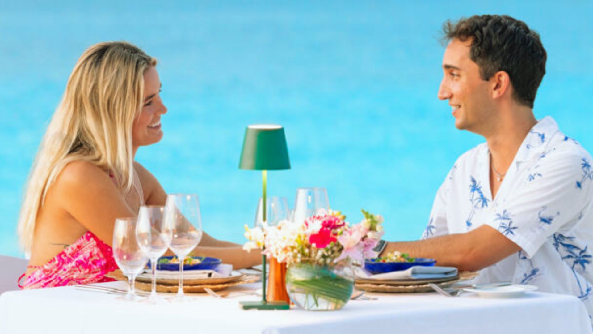 A man and woman sit at a table, enjoying a meal with a scenic view of the ocean in the background.