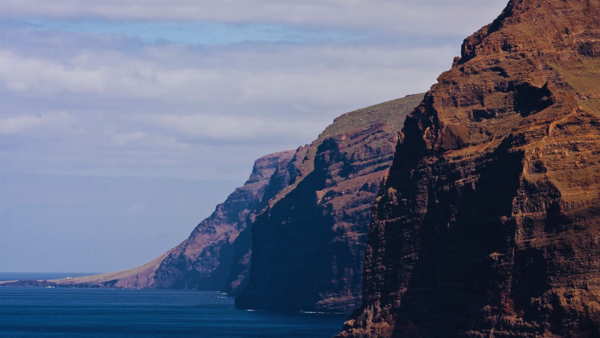 A towering cliff with a serene body of water visible in the background under a clear sky.