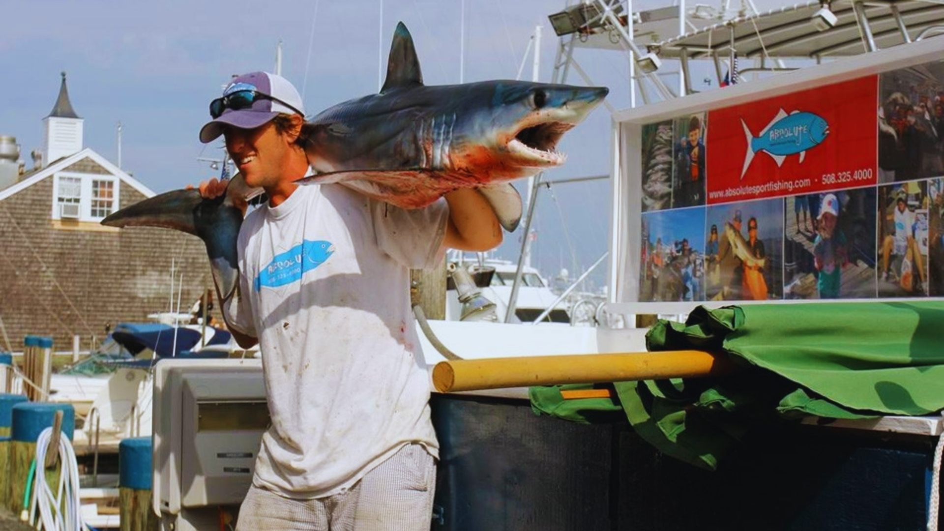 A man on a boat displays a large shark he has just caught, showcasing his fishing achievement.