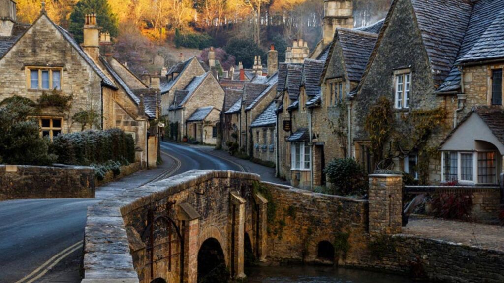 Scenic view of Bibury village in the Cotswolds, England, featuring traditional stone cottages and lush greenery.