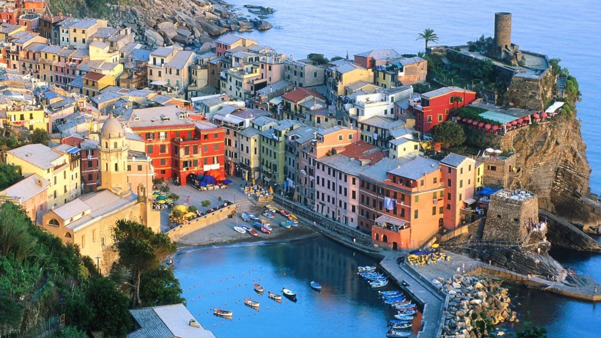 A picturesque coastal town with boats docked in the serene water, showcasing vibrant buildings and a clear blue sky.