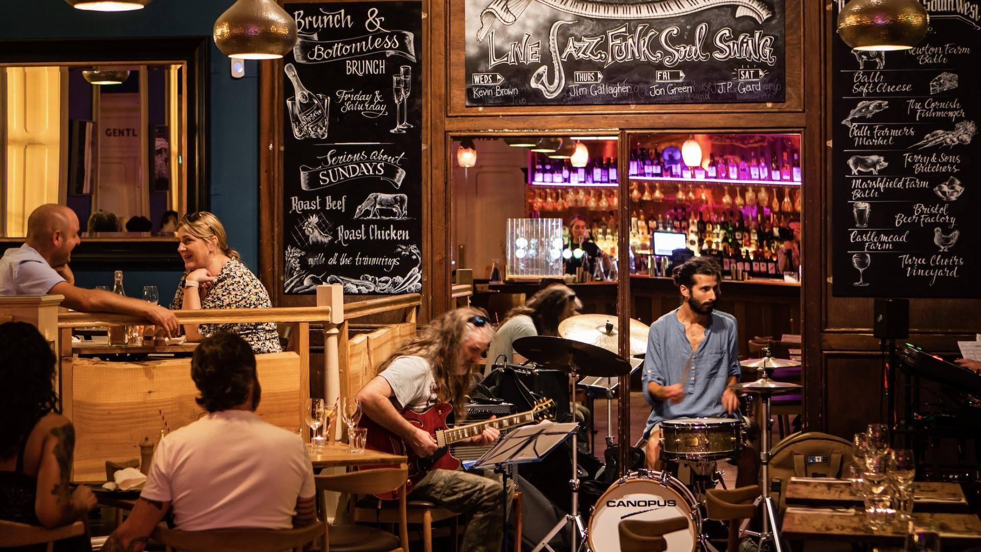 A group of people dining at tables in a restaurant, engaged in conversation and enjoying their meals.