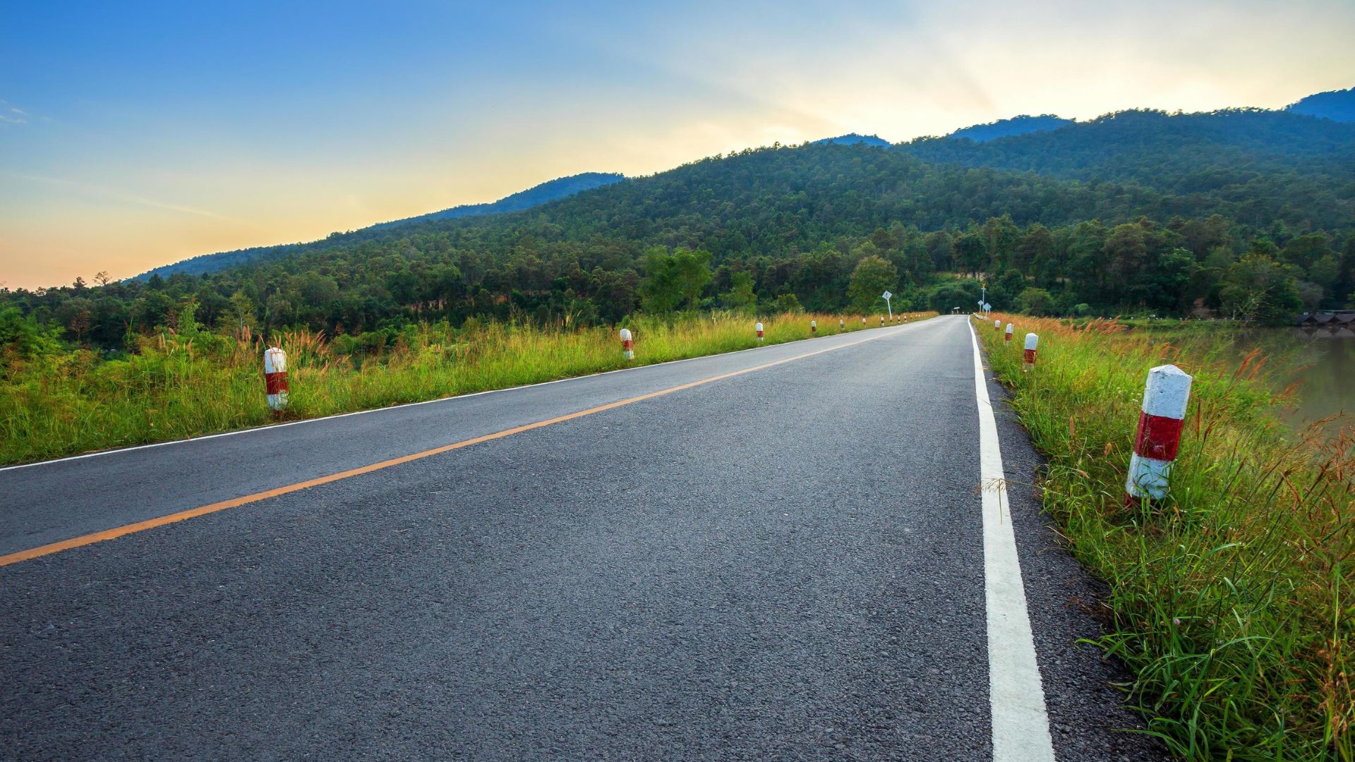 An empty road stretches ahead, with a majestic mountain rising in the background under a clear blue sky.