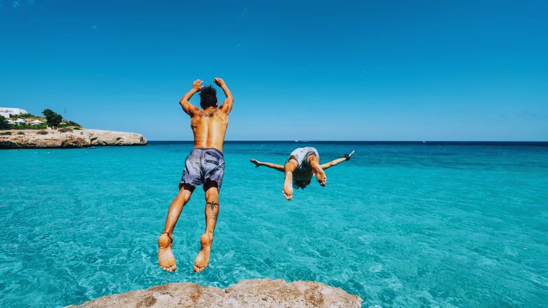 Two individuals leaping into the ocean from a rocky cliff, capturing a moment of adventure and excitement.