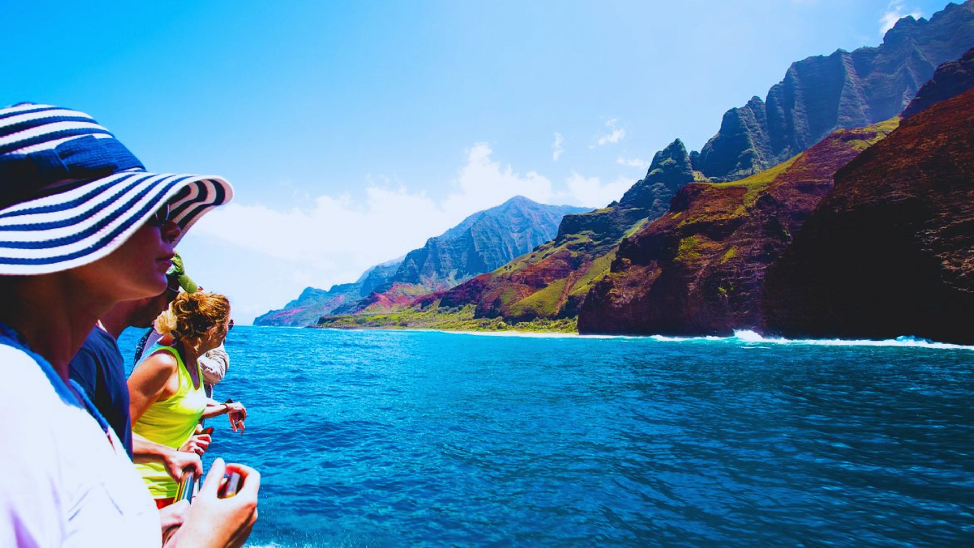 A woman and a man stand on a boat's side, gazing out at the vast ocean under a clear blue sky.