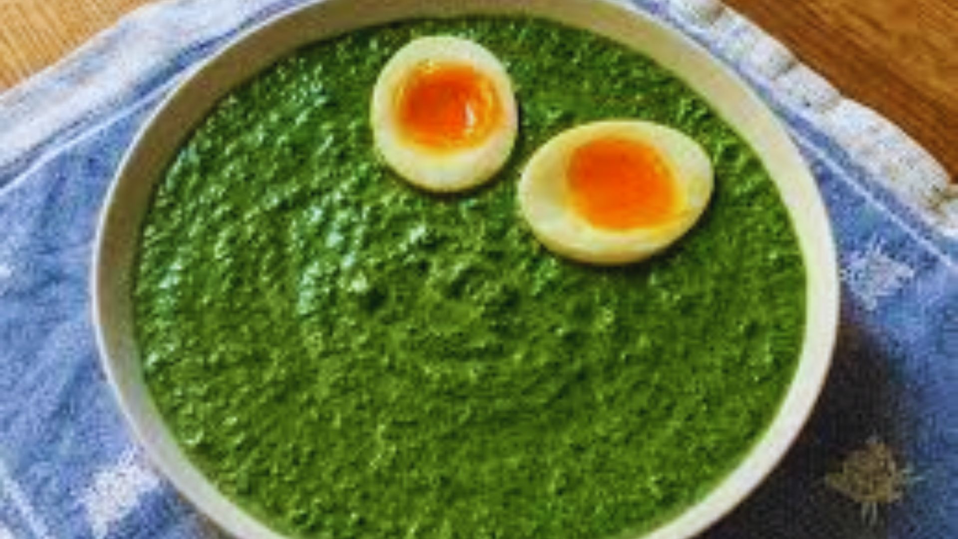 A bowl of vibrant green soup topped with two soft-boiled eggs, creating a colorful and appetizing dish.