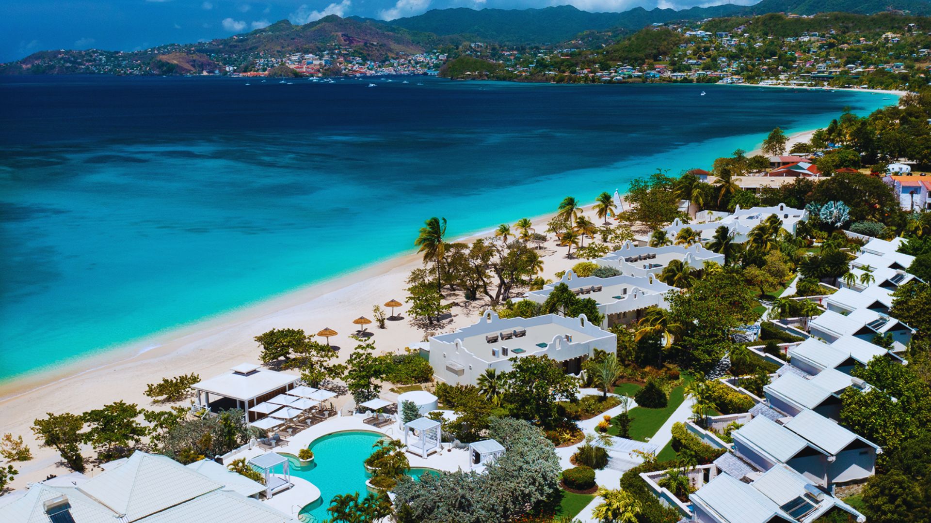 Aerial view of a tropical beach resort with turquoise waters, white sandy beach, and lush greenery. White villas and pools are nestled along the shoreline.