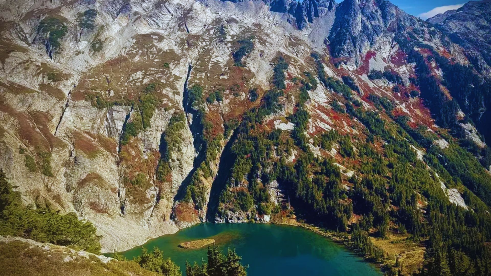 Majestic mountain landscape with steep rocky cliffs and vibrant green vegetation. A clear turquoise lake nestles below, conveying serene natural beauty.