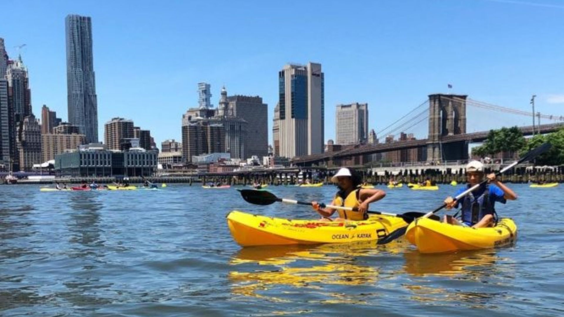 A person kayaking in the East River with the New York City skyline in the background on a sunny day.